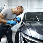 Male technician applying ceramic coating to a car’s exterior at Exclusive Car Care Abu Dhabi for enhanced gloss and paint protection.